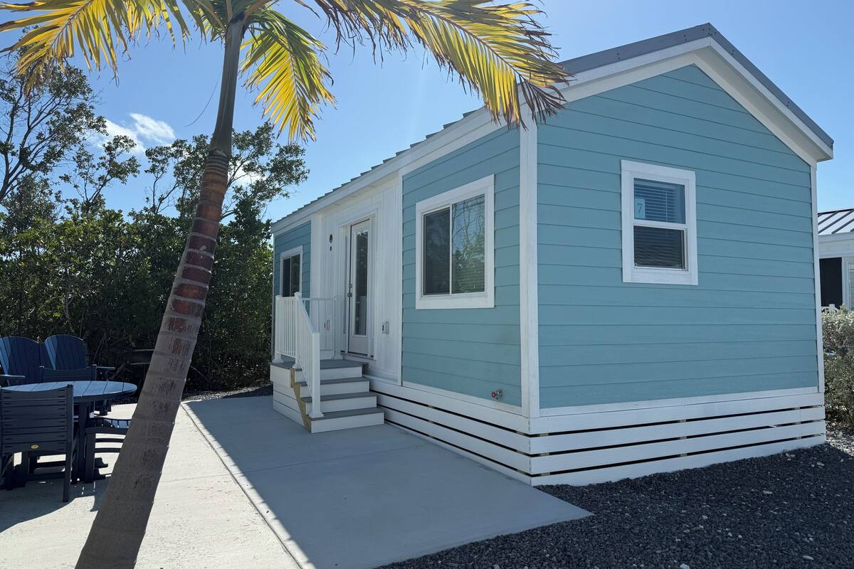 A small, single-story house with a porch, a palm tree, and a clear blue sky.