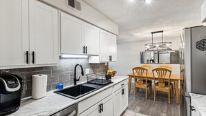 Cozinha moderna com armários brancos, uma pia preta e uma área de jantar com cadeiras de madeira.