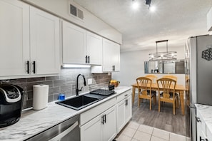 A modern kitchen with white cabinets, a black sink, and a dining area with wooden chairs.
