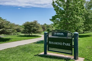 A sign for Denver Parks & Recreation Rosamond Park with a clear pathway and lush greenery.