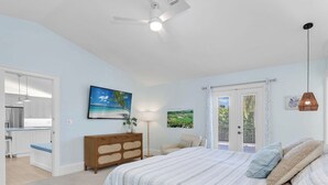 Quarto com cama, penteadeira, televisão e porta que dá para uma varanda.