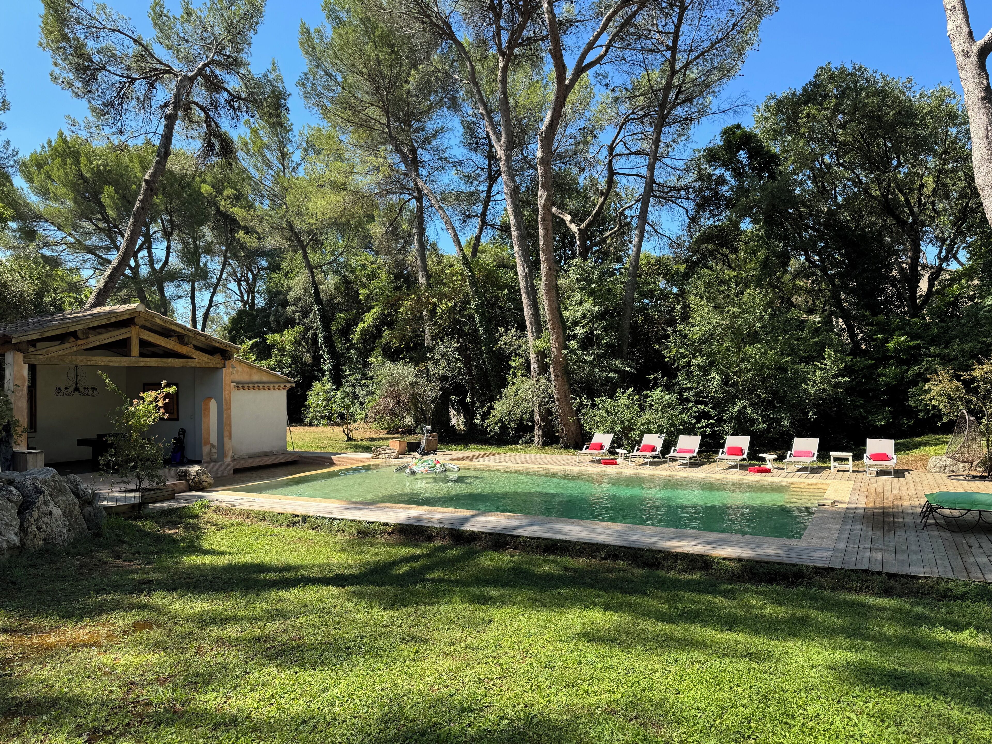 A backyard with a swimming pool, lounge chairs, and a small pavilion.