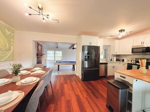 A modern kitchen with white cabinets, a stainless steel refrigerator, and a pool table in the dining area.