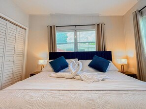 A hotel room with a bed, two bedside lamps, a window with curtains, and a headboard.