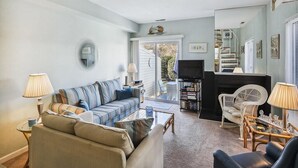 Una sala de estar con sofá, mesa de centro, sillas, televisor y estantería.
