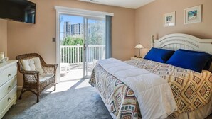 Un dormitorio con cama, silla, cómoda, televisor y balcón con vista.