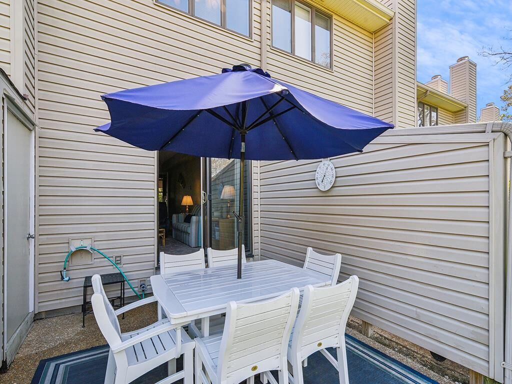 A patio with a table and chairs, a blue umbrella, and a clock on the wall.