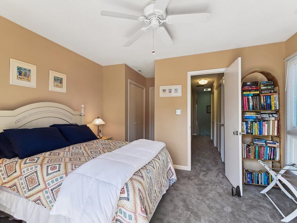 Un dormitorio con cama, ventilador de techo, estantería y una puerta que da a otra habitación.