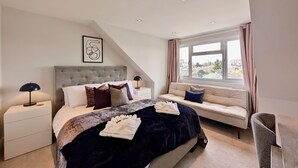 A bedroom with a bed, a nightstand, a sofa, a window with curtains, and a view of the outside. - Bright Ensuite Room in Shared Wandsworth Flat (London)