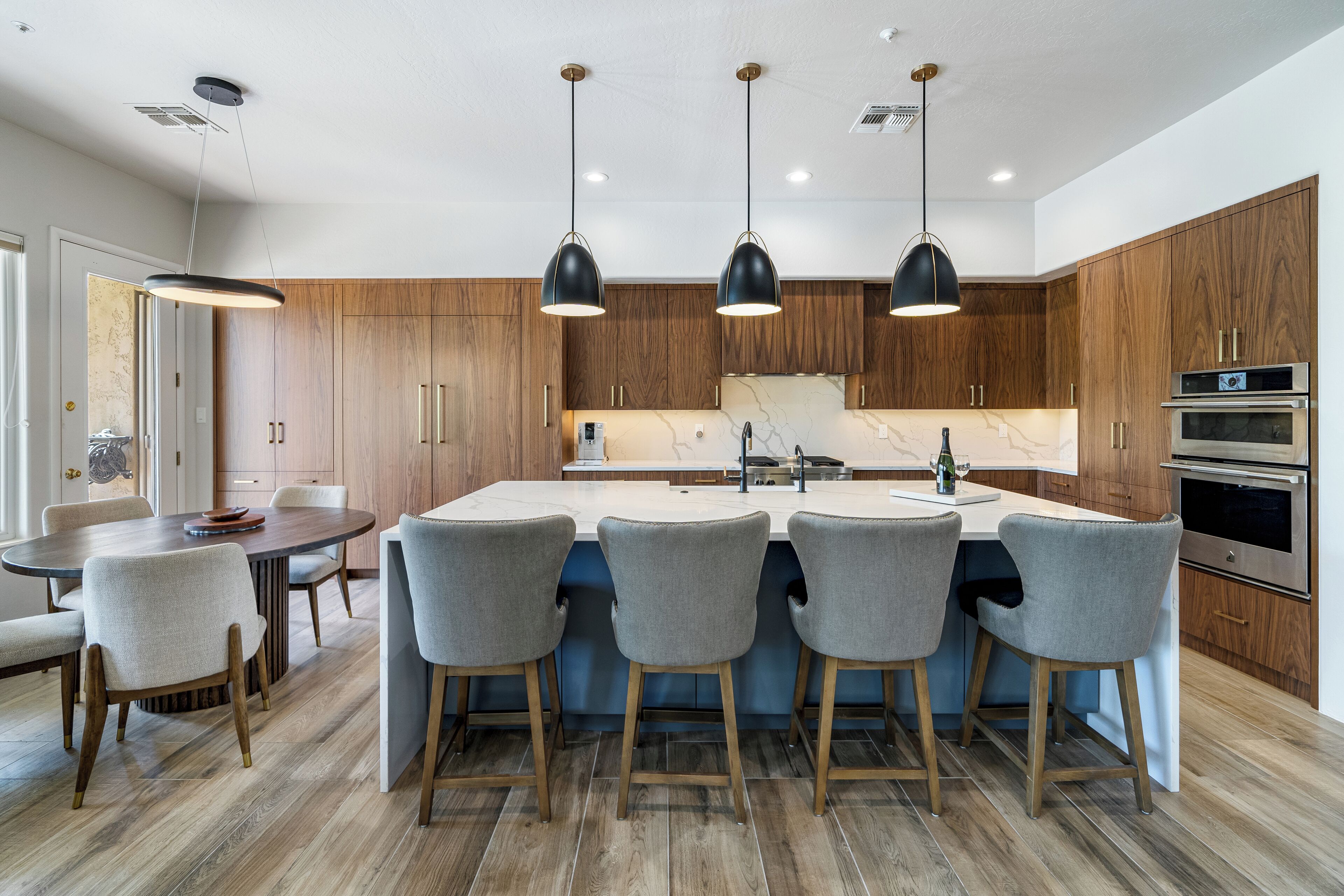 A modern kitchen with wooden cabinets, a central island with bar stools, pendant lighting, and built-in appliances.