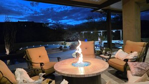 Un espace extérieur aménagé avec une table ronde dotée d’un foyer, entouré de fauteuils confortables et d’un patio couvert.