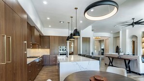 Une cuisine moderne avec des meubles en bois, un îlot en marbre, des luminaires suspendus et un ventilateur de plafond.