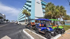 Um hotel moderno com fachada geométrica marcante, área de estacionamento com carrinhos de golfe e palmeiras por perto.