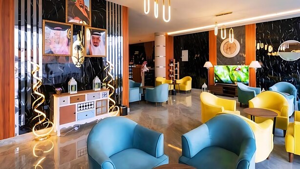 A modern hotel lobby with blue and yellow seating, a TV, and a decorative wall with framed pictures. - Pearly Hotel (Abha)