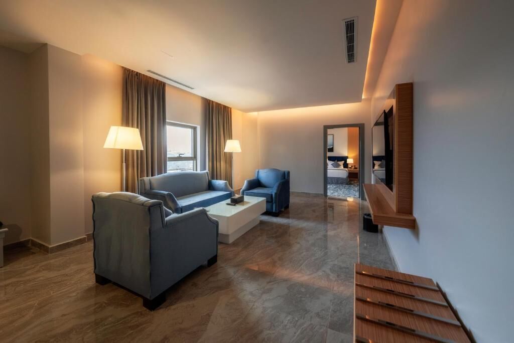 A modern hotel room with a sofa, armchairs, a coffee table, and a staircase.