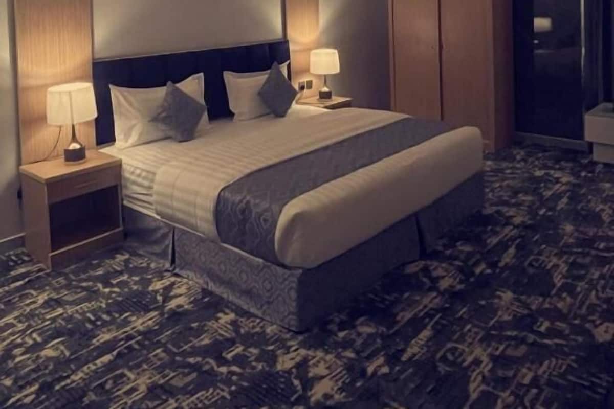 A hotel room with a large bed, two bedside tables with lamps, a wardrobe, and a framed picture on the wall.