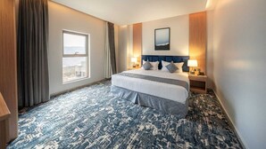 A hotel room with a large bed, two bedside tables, a window with curtains, and a cityscape view. - Pearly Hotel (Abha)