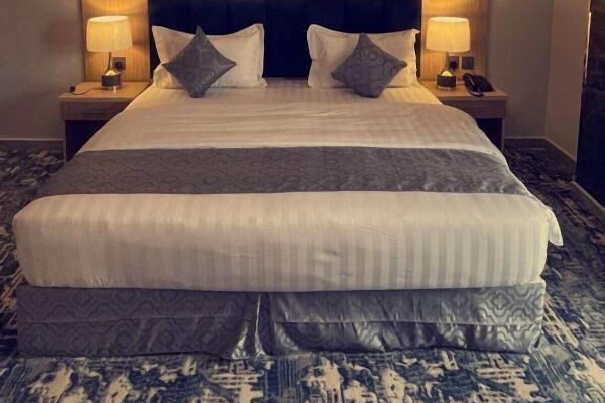A hotel room with a large bed, two bedside tables with lamps, a framed picture on the wall, and a patterned carpet.