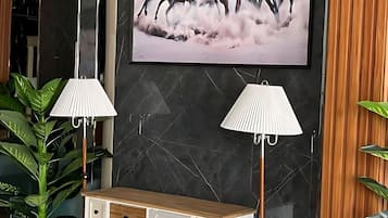 A modern interior with a marble wall, a mounted TV, a white console with drawers, and two floor lamps.