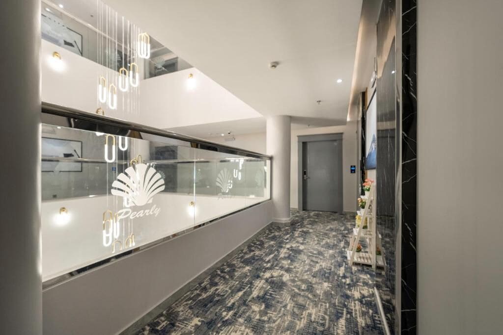 A hallway with a glass partition displaying the 'Pearly' logo, a marble-patterned floor, and a white reception desk.