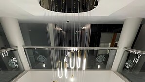 A modern interior with a central hanging light fixture, glass railings, and a blue-toned entrance. - Pearly Hotel (Abha)