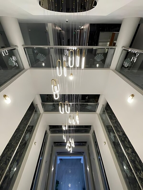 En modern interiör med en centralt placerad hängande lampa, glasräcken och en entré i blå nyanser.