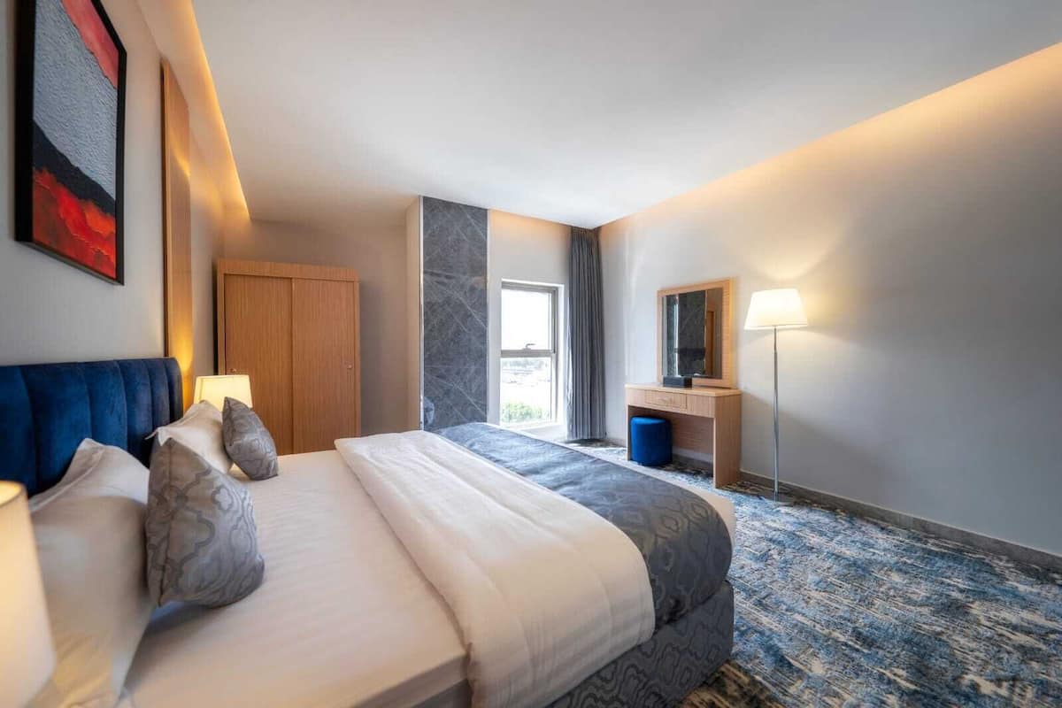 A hotel room with a bed, bedside table, lamp, wardrobe, and a large window.