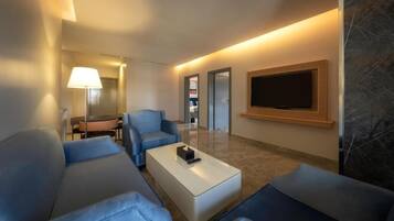 Una habitación de hotel moderna con sofá, una mesa de centro, un televisor de pantalla plana montado en la pared y una lámpara.