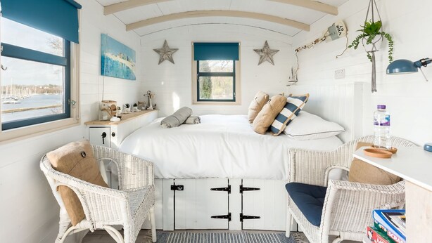 Un dormitorio con cama, dos sillas de mimbre, un escritorio, una ventana con vista a barcos y decoraciones con motivos de estrellas.
