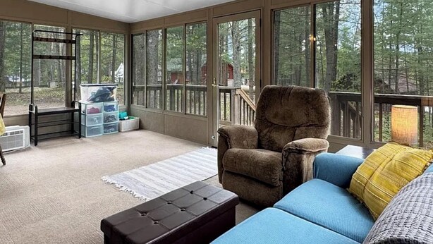 A sunroom with large windows, a cushioned chair, a blue sofa, and storage bins. - Grace on the Lake-Little Red Cabin-Perch Lake, MI (South Boardman)