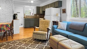 A spacious living room with a sofa, armchair, and a dining area with a table and chairs. - Grace on the Lake-Little Red Cabin-Perch Lake, MI (South Boardman)