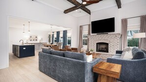 A modern living room with a fireplace, a large sofa, and a television mounted on the wall. - New Gameday Getaway AU Club Home: 3BR + Outdoor Living (Auburn)