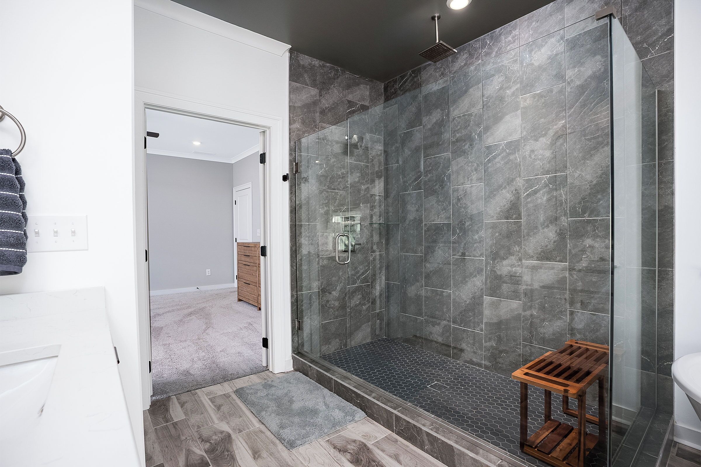 Ein modernes Badezimmer mit einer gläsernen Duschkabine, einem Holzschemel und einer Marmorwand.
