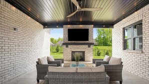 A covered patio with a brick fireplace, wicker furniture, and a ceiling fan. - New Gameday Getaway AU Club Home: 3BR + Outdoor Living (Auburn)