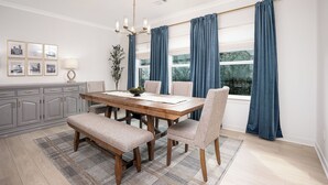 A dining room with a wooden table, chairs, a bench, a chandelier, curtains, and framed pictures on the wall. - New Gameday Getaway AU Club Home: 3BR + Outdoor Living (Auburn)