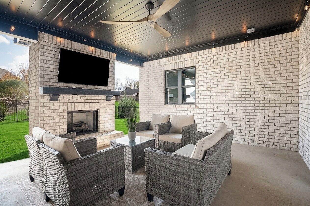 Un patio al aire libre con mobiliario de mimbre, un televisor de pantalla plana y una chimenea de ladrillo.