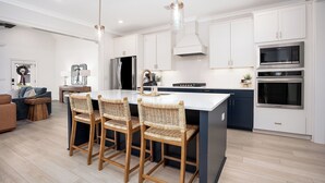A modern kitchen with a central island, bar stools, and built-in appliances. - New Gameday Getaway AU Club Home: 3BR + Outdoor Living (Auburn)