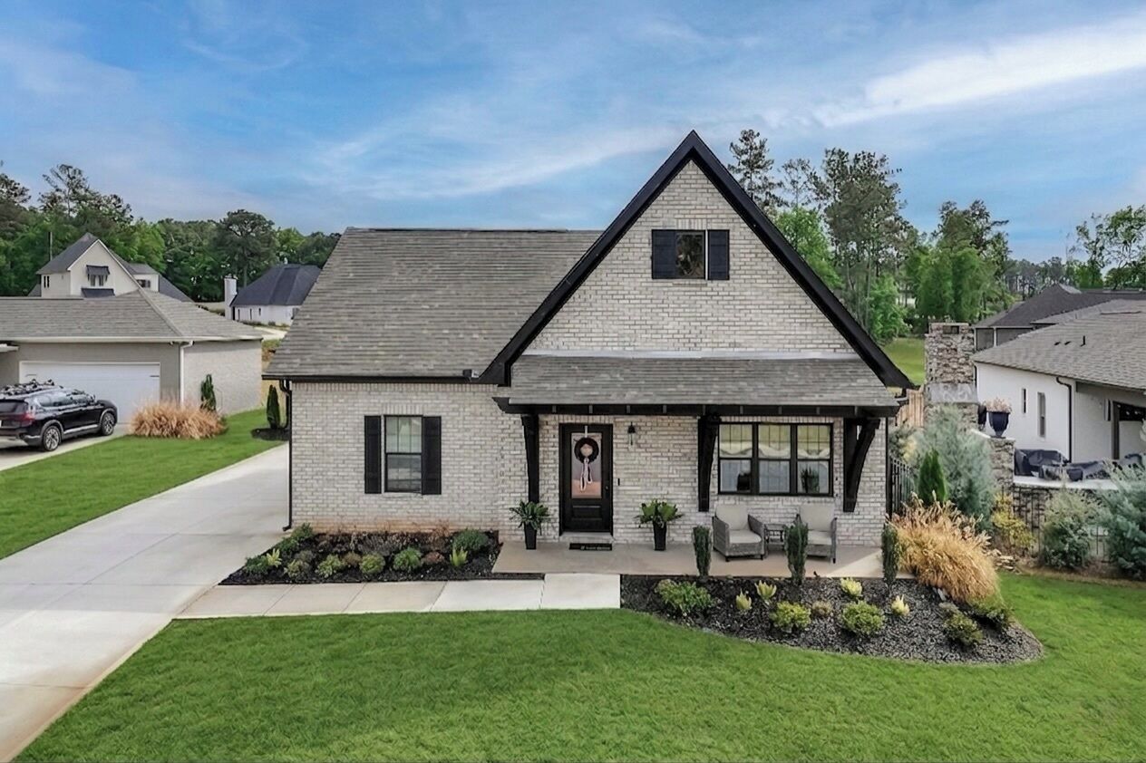 A modern two-story house with a brick facade, a dark roof, and a front porch with seating.