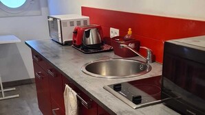 A kitchen with a sink, stove, microwave, and red cabinets. - Comfortable apartment in private property overlooking flower garden (Lys-Haut-Layon)