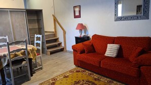 A room with a wooden staircase, a red sofa, a small table with a lamp, and a patterned rug. - Comfortable apartment in private property overlooking flower garden (Lys-Haut-Layon)