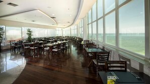 Un comedor amplio con mesas y sillas, ventanas grandes y vista al agua.