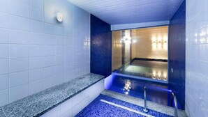 Un baño moderno con pared de azulejos azules, encimera de granito y jacuzzi con mampara de vidrio.