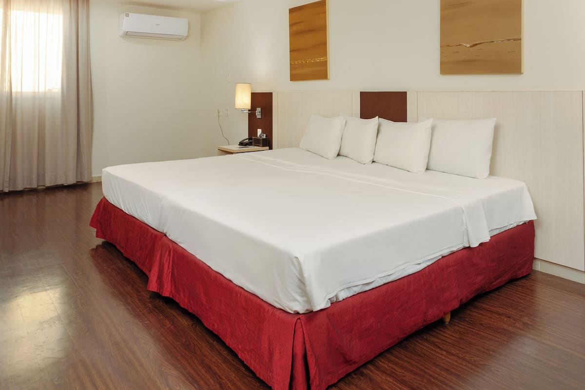 Habitación de hotel con una cama grande, una mesita de noche, un equipo de aire acondicionado y una obra de arte colgada en la pared.