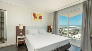 Habitación de hotel con cama, mesita de noche, lámpara, un cuadro y balcón con sillas.