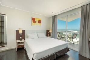 A hotel room with a bed, a nightstand, a lamp, a painting, and a balcony with chairs. - Royal Kingdom  (Macaé)