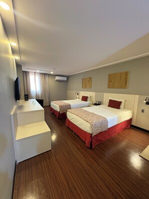 A hotel room with two beds, a desk, and an air conditioning unit.