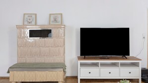 Ein Zimmer mit Fernseher auf einem Holzboden, einem beige gefärbten Schrank mit Fenster und einem Bett mit grüner Decke.