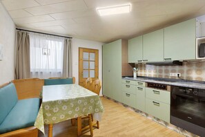 Kompakti keittiö, jossa on ruokailutila. Tilaan kuuluu pöytä, jossa on kukallinen pöytäliina, puiset tuolit ja sisäänrakennettu uuni.