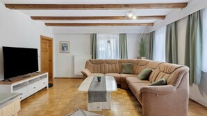Ein Wohnzimmer mit Ecksofa, Flachbildfernseher, Couchtisch aus Holz und Radiator.