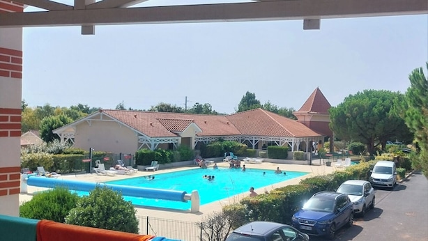 A swimming pool with people, a covered area, and parked cars. - Appt T4 Residence Le Cordouan 3* pool side (Soulac-sur-Mer)
